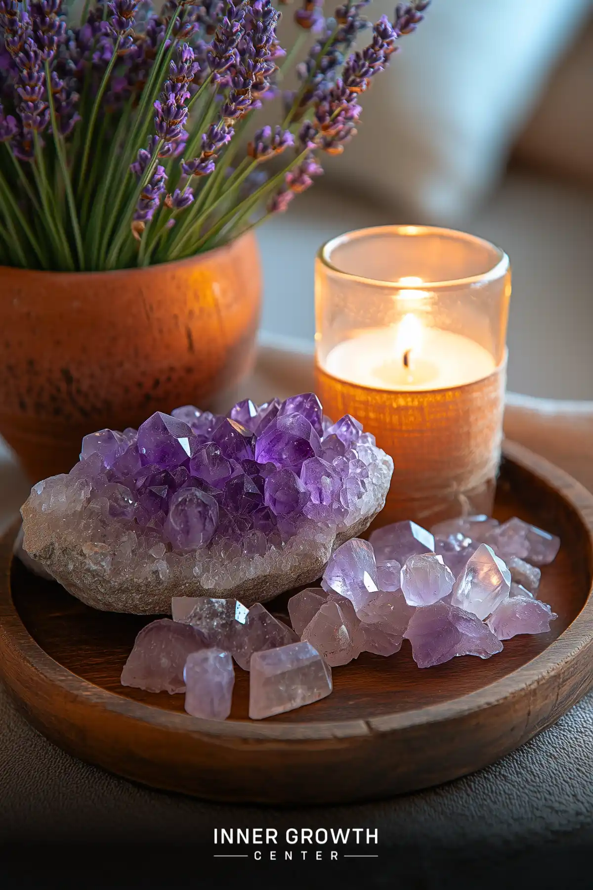 A wooden bowl displays amethyst crystals and a glowing candle alongside fresh lavender, creating a peaceful meditation setting.