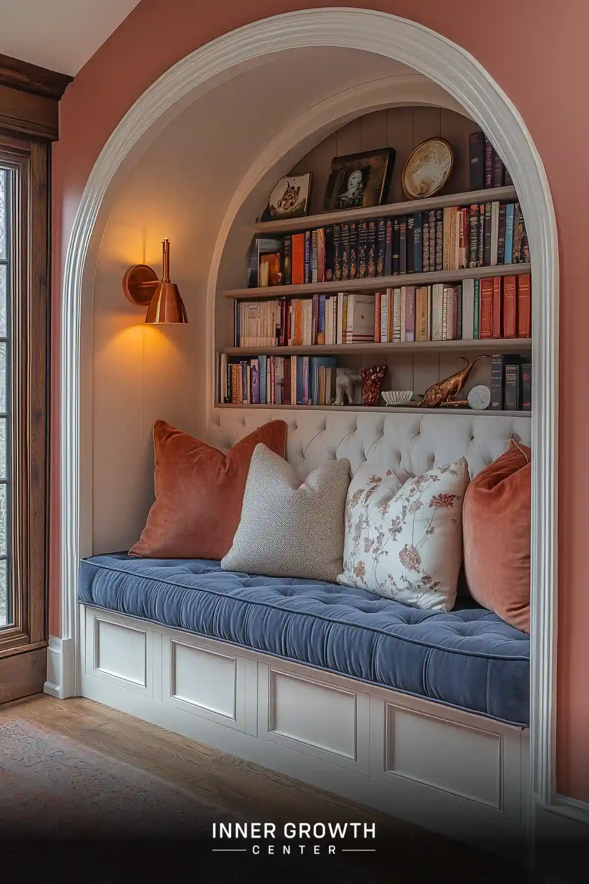 A built-in window seat nestled within a white arched alcove features a blue tufted cushion, coral pillows, and built-in bookshelves.