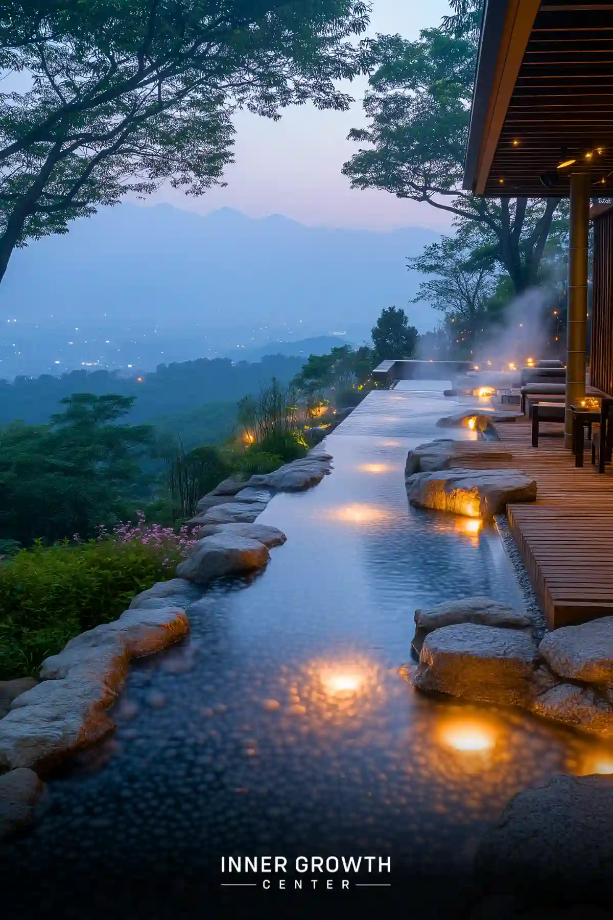 Illuminated water feature on a wooden deck overlooking misty mountains at dusk.